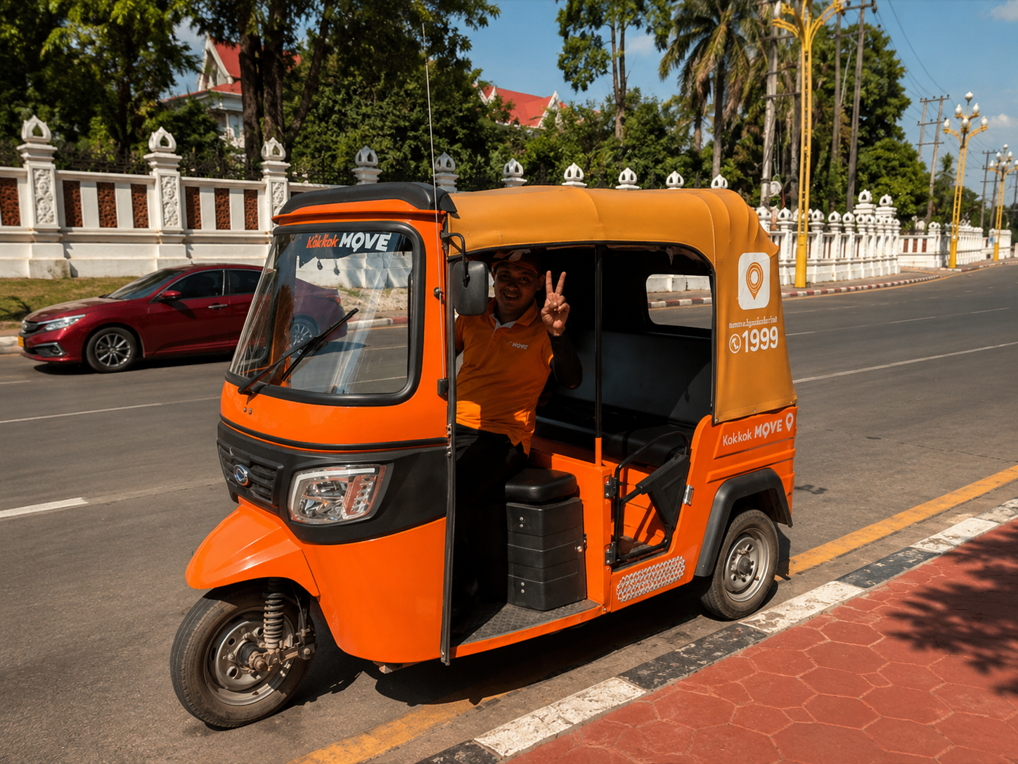 An orange Kok Kok MOVE tuk-tuk with its driver on a Vientiane street